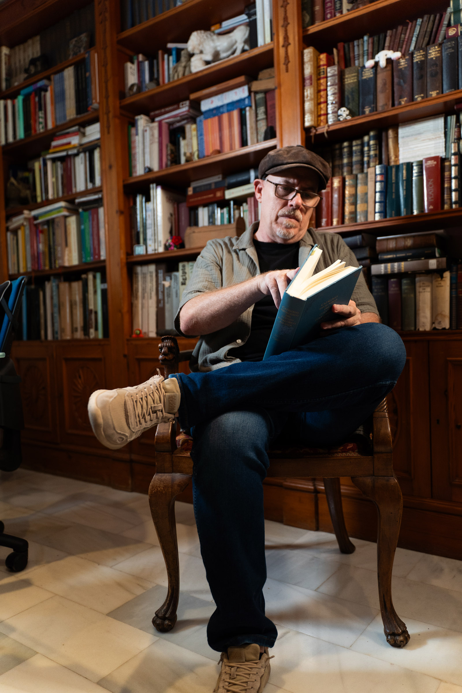 Poti de Cai sentado leyendo un libro ante las estanterías de su biblioteca